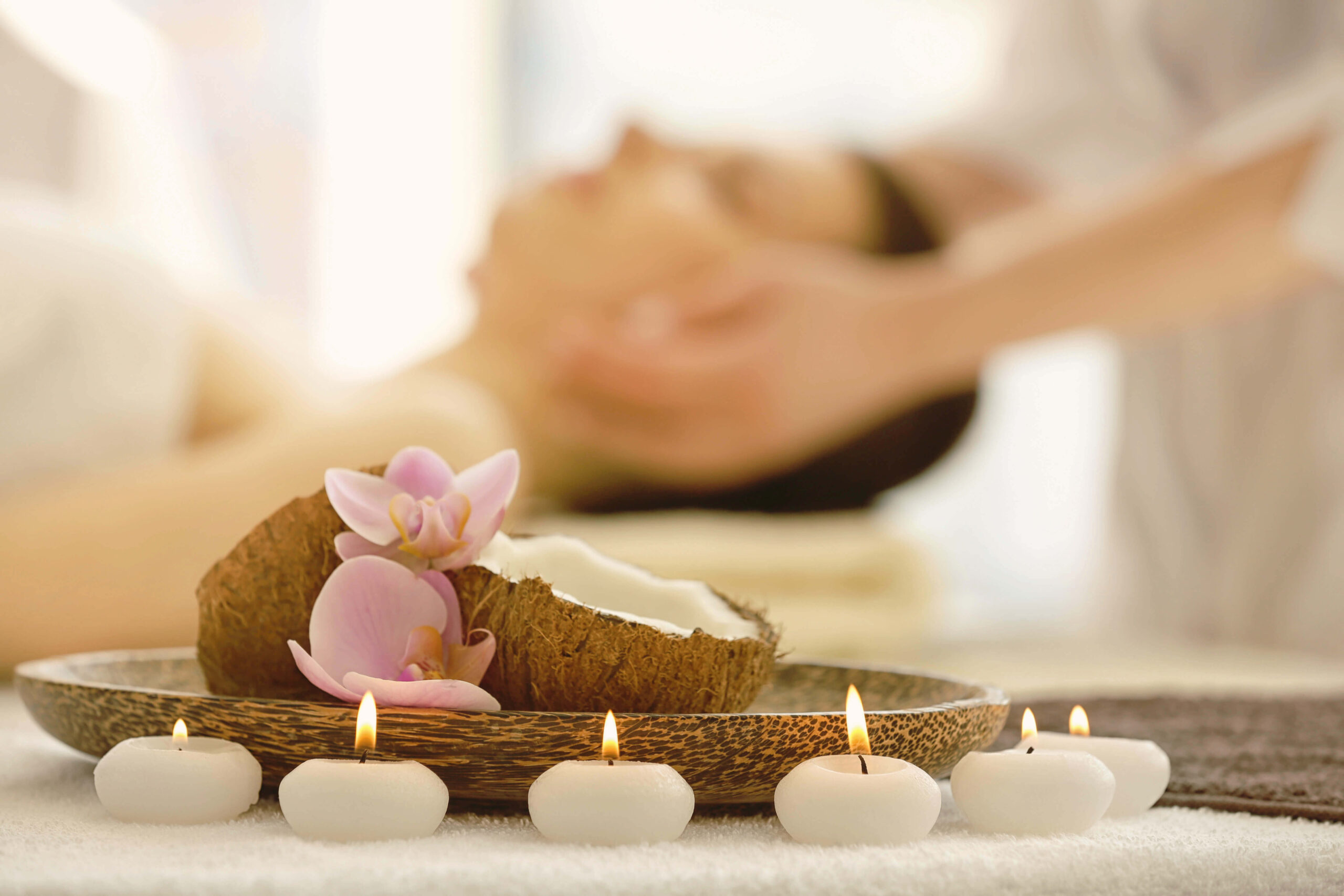 Tealight candles and pink flowers in front of a person being given a relaxing face and temple massage.