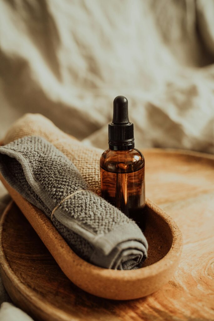 Warm hand towels rolled up next to massage oil in wooden bowl.